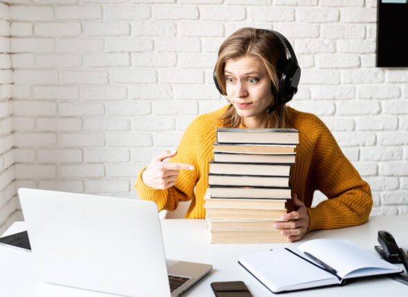 Cursuri 423 Distance-Learning-E-Learning-Young-Woman-Black-Headphones-Using-Laptop-Holding-Stack-Books